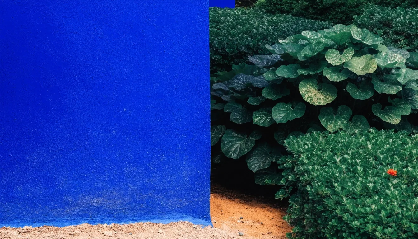 A cobalt garden wall beside vivid green foliage, ochre earth and a bright flower accent