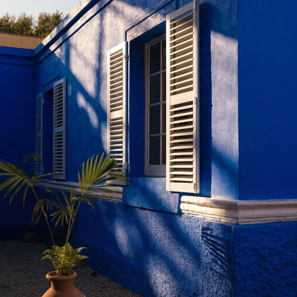 The cobalt studio-villa facade with white Art Deco shutters and framed openings in raking afternoon light