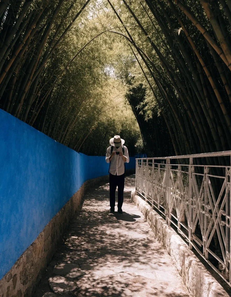 A visitor photographing a shaded alley between a cobalt wall and a white railing in the Majorelle Garden